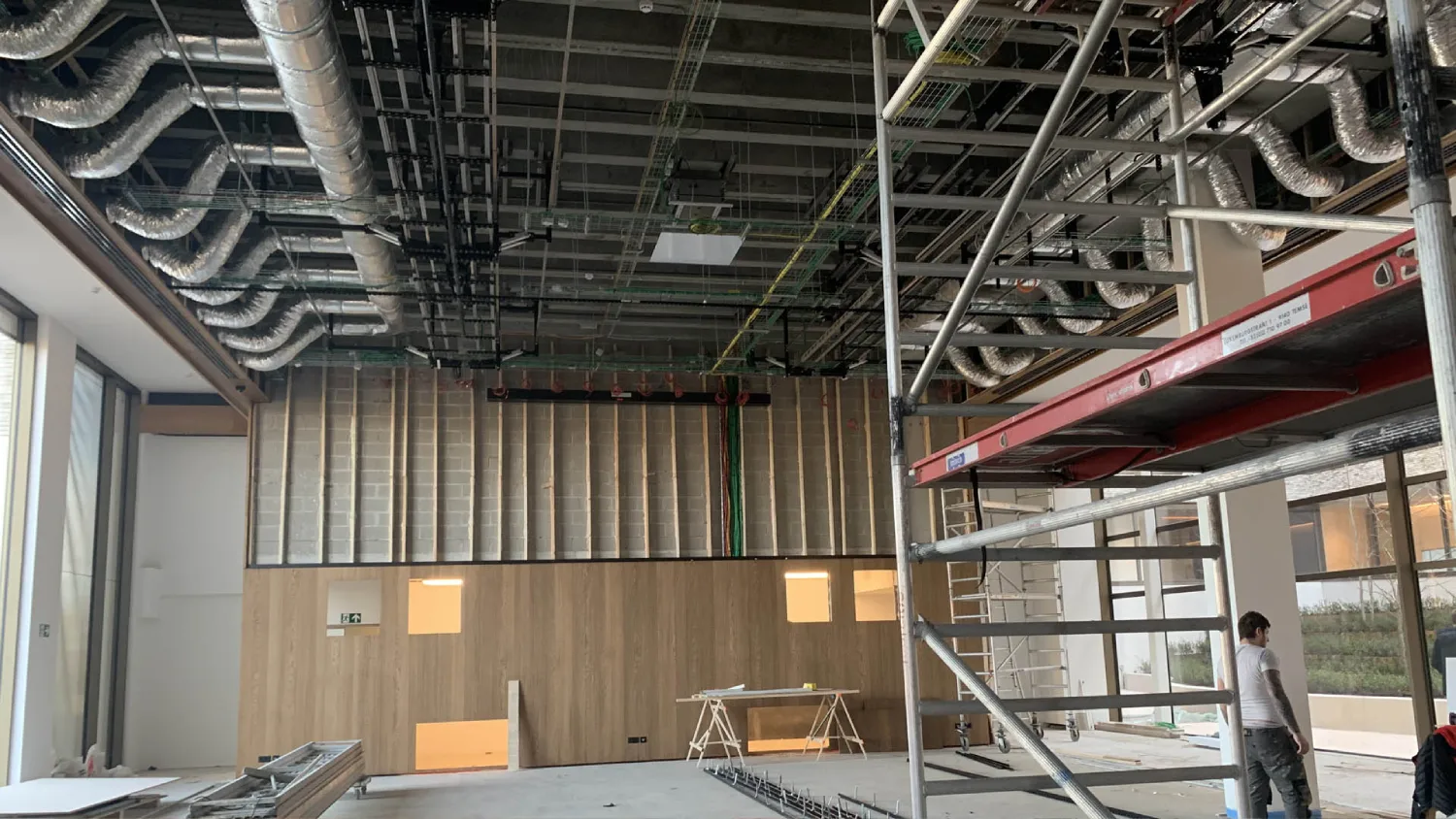 Installation technique d'un plafond LED matriciel dynamique et de son câblage dans un grand hall événementiel moderne. Une nacelle ciseau orange est déployée avec deux techniciens fixant les modules lumineux.